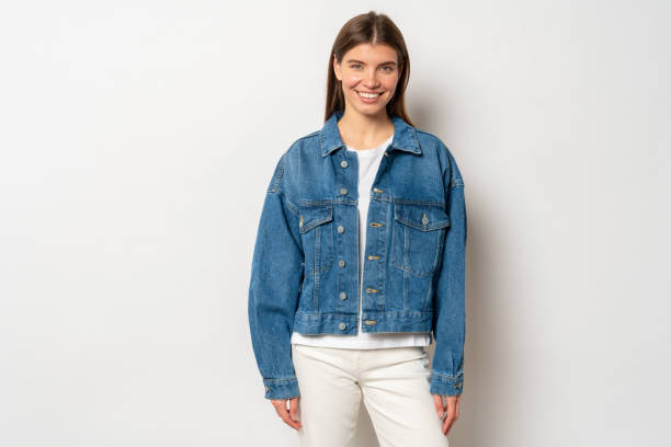 Carefree girl standing against light blank studio background in denim jacket smiling