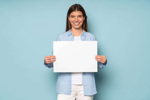 파란색 배경 위에 복사 공간이있는 흰색 빈 배너를 들고있는 여성 임원 관리자 - businesswoman advertise placard advertisement 뉴스 사진 이미지