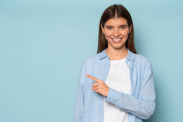 istock Happy female office worker pointing index finger away on blue studio copy space wall 1406335648