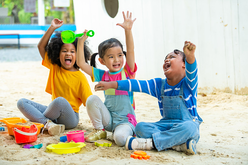 Happy children kid playing together at playground on summer vacation. Group of Diversity little child boy and girl friends enjoy and fun outdoor activity lifestyle playing sand with toy at playground