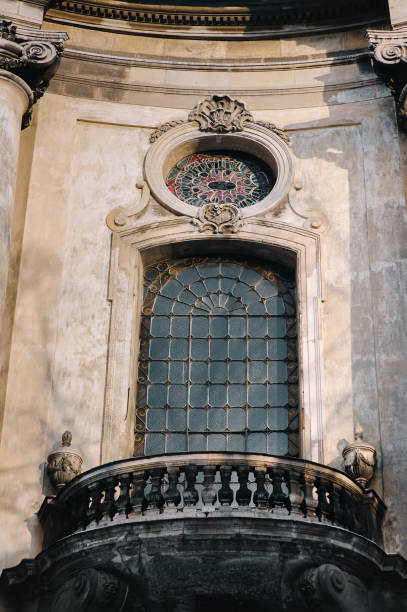 istock Beautiful antique baroque round window framed by decorative stucco with a balcony and balustrade below on a beige wall background. Dominican Cathedral Monastery. Lviv, Ukraine. 1406337654