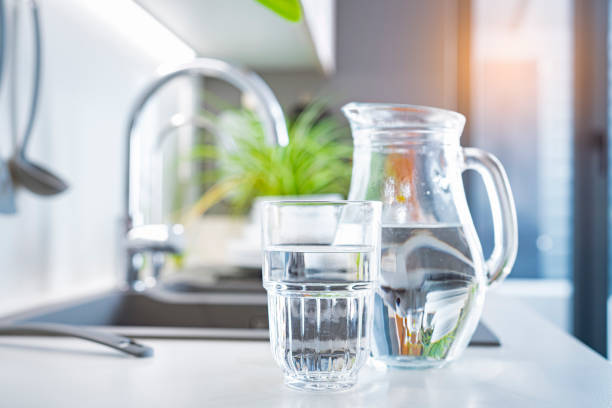 glas wasser und krug auf der küchentheke - destilliertes wasser stock-fotos und bilder