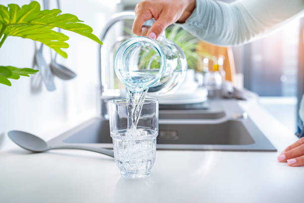 Close up of a woman hand pouring drinking water from jug to a glass on kitchen counter. High resolution 42Mp indoors digital capture taken with SONY A7rII and Zeiss Batis 40mm F2.0 CF lens