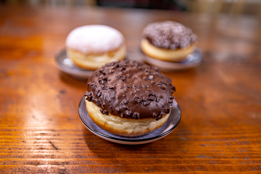 Three donuts on the table. The focus is on the donut with chocolate topping and chocolate crumbs in the foreground.