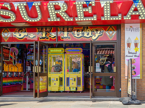Whitby, UK. June 15, 2022.  An amusement arcade with a gaming machine on one side and two machines with fluffy toys in the centre. An ice cream sign is on a wall.