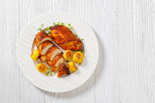 grilled chicken breasts with browned new potatoes on white plate, horizontal view from above, flat lay, free space