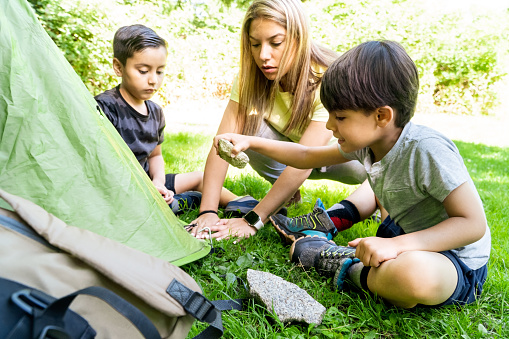 multhietnic latin and caucasian children nailing tent pegs on a summer camp with woman instructor. learning to pitch a tent. Vacation concept