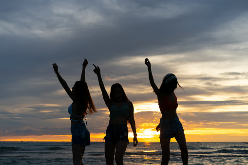 Silhouette Group of Young Asian woman in dancing and playing together on the beach at summer sunset. Happy female friends enjoy and fun outdoor activity lifestyle on holiday travel vacation at the sea