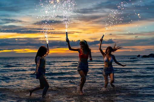Group of Young beautiful Asian woman having fun dancing and playing sparklers together on tropical island beach in summer night. Happy female friends enjoy outdoor lifestyle nightlife on holiday travel vacation trip