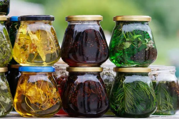 Photo of glass jars with favoured honey - with linden, herbs and pine needles, close-up