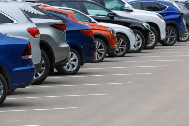 Photo of row of different color cars on asphalt parking lot at cloudy summer day