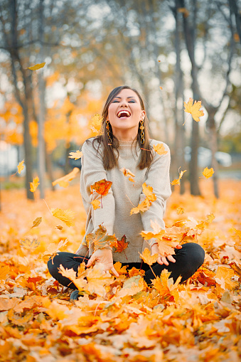 Laughing young woman having fun in autumn park playing with fallen leaves, copy space.