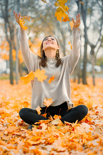 Happy mixed race young woman smiling joyful throws up autumn leaves outside in fall forest, copy space.