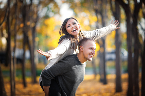 Enamoured young couple fool around in autumn outdoor. A man rolls a woman on his back, and she depicts a flight.