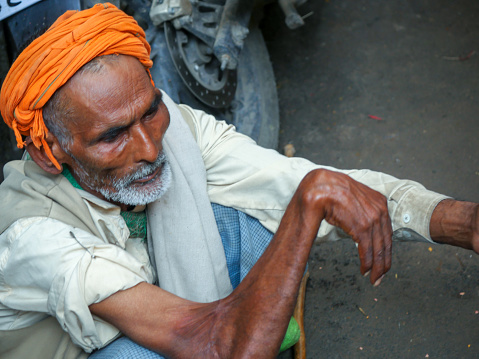 An elderly pilgrim, unshaven, wearing a white turban, and a grey, brown mantle. This man was taking part of a food distribution to the poor. Photo taken during Kumbh Mela 2019 in Prayagraj (Allahabad), India. \nKumbh Mela or Kumbha Mela is a major pilgrimage and festival in Hinduism, and probably the greatest religious festival in the World. It is celebrated in a cycle of approximately 12 years at four river-bank pilgrimage sites: the Allahabad (Ganges-Yamuna Sarasvati rivers confluence), Haridwar (Ganges), Nashik (Godavari), and Ujjain (Shipra). The festival is marked by a ritual dip in the waters, but it is also a celebration of community commerce with numerous fairs, education, religious discourses by saints, mass feedings of monks or the poor, and entertainment spectacles. Pilgrims believe that bathing in these rivers is a means to cleanses them of their sins and favour a better next incarnation.