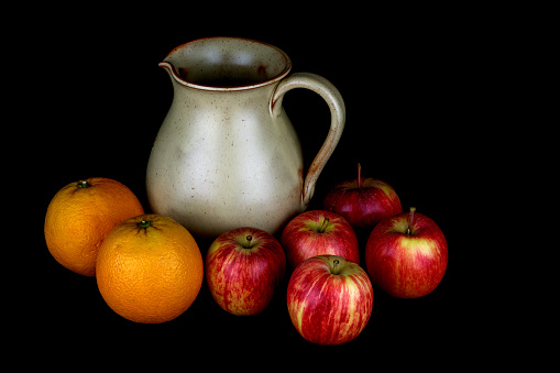 Earthenware jug with apples and oranges isolated on a black background