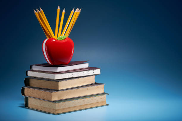 apple shaped pencil holder with pencils with stack of books against blue background
