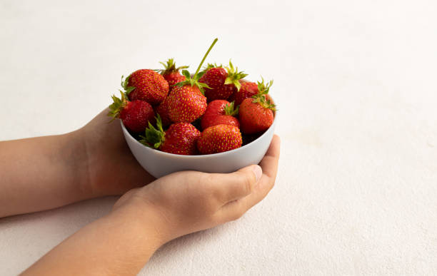 istock A child's hand holding strawberries on a light background 1406371078