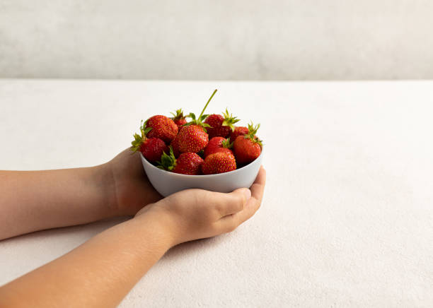 istock A child's hand holding strawberries on a light background 1406371079