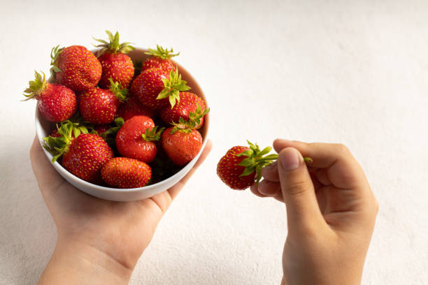 istock A child's hand holding strawberries on a light background 1406371113