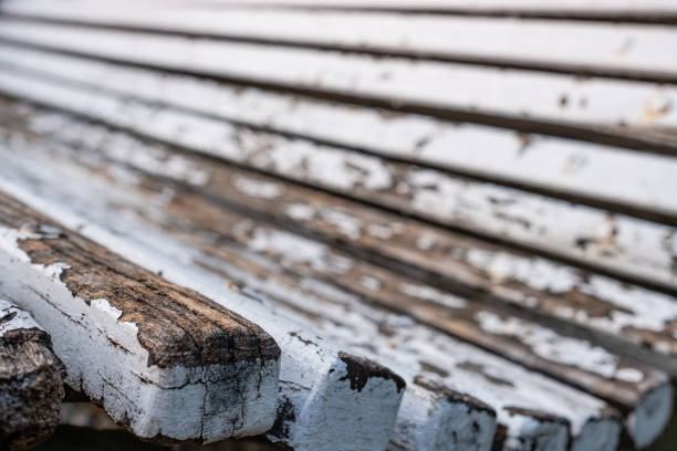 Close-up shot of an old weathered wooden bench. Close-up of the edge, details of peeling white paint and wood material.\nSide perspective view, selective focus.