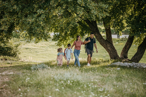 Family of four, mother and father with her little son and daughter taking a walk together on a meadow in nature.