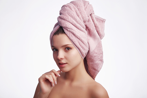 Young attractive woman with towel on her head looks at the camera and smiles on white background with copy space for text. Face care and hair concept