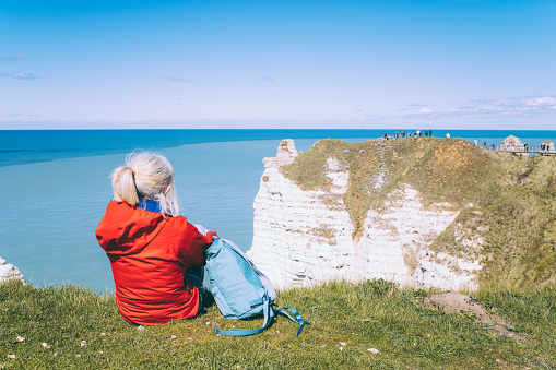 Mature female hiker on the clifftop at Etretat on the Normandy coast of France beside the natural arch known as La Manneporte.