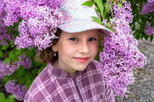 Portrait of a child 7 years old, Girl in the lilac bushes in the summer in the city garden. close-up