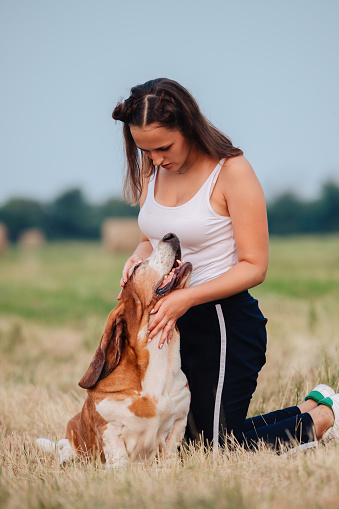 A young adult girl walks with a Basset Hound dog in nature.