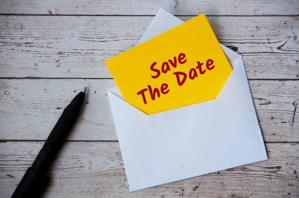 istock Save the date text on yellow notepad in an envelope with pen and wooden desk background. Reminder concept 1406382497
