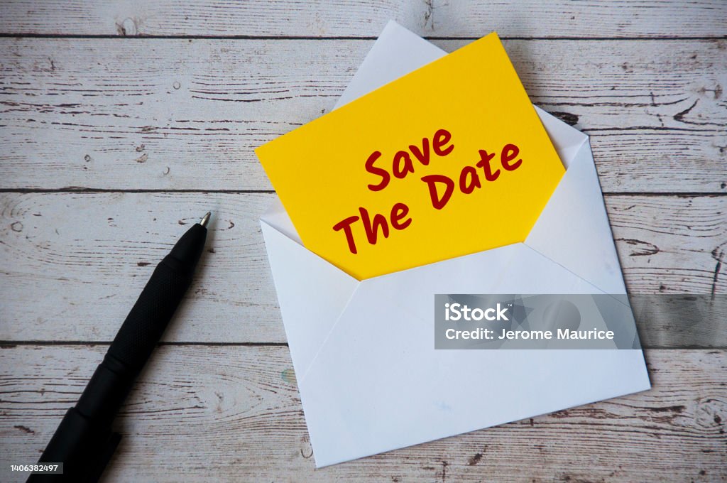 Save the date text on yellow notepad in an envelope with pen and wooden desk background. Reminder concept Save the date text on yellow notepad in an envelope with pen and wooden desk background. Making a Reservation Stock Photo