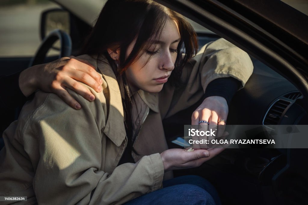 problems and depression in young people a young beautiful girl is sitting in the passenger seat in the car, she is depressed in her hand a handful of psychotropic pills 20-24 Years Stock Photo