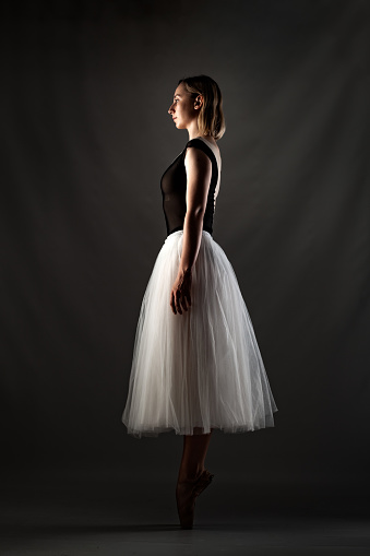 ballerina with a white dress and black top posing on gray background