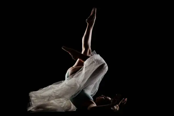 ballerina with a white dress and black top posing on black background. side lit silhouette