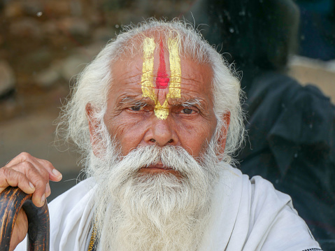 This Sadhu uses ashes of cremated remains to prepare specific white color of his makeup.\nIn Hinduism, sadhu, or shadhu is a common term for a mystic, an ascetic, practitioner of yoga (yogi) and/or wandering monks. The sadhu is solely dedicated to achieving the fourth and final Hindu goal of life, moksha (liberation), through meditation and contemplation of Brahman. Sadhus often wear ochre-colored clothing, symbolizing renunciation.