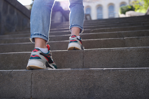Female legs in sports sneakers going up stairs closeup. Hiking in city concept