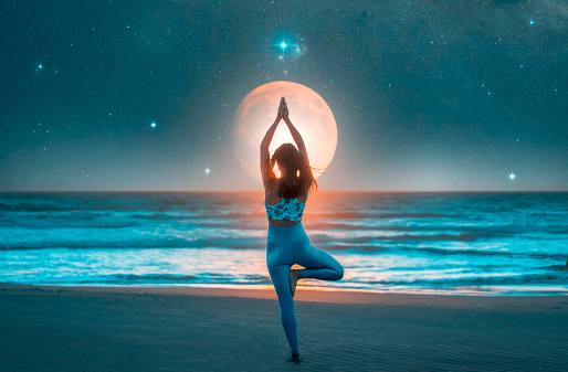 silhouette of a woman doing yoga on the shore of the beach with the moon in the background
