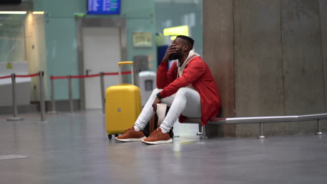 Exhausted African man on a long night connection at airport, waiting for a plane sitting in terminal