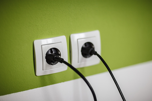 Electricity plugs in the socket on green wall