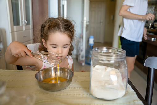 cute baby girl scrambling eggs making cakes with her mother in the kitchen