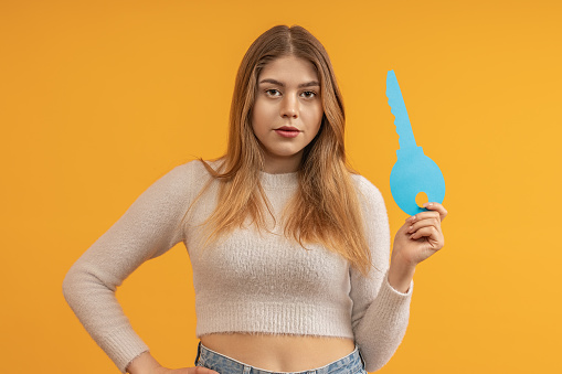 beautiful young woman showing big paper key on color background