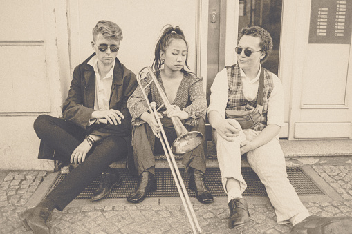 Portrait of three young adults. They are casually sitting on the entrance step of a house in the big city.