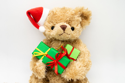 A stuffed toy Teddy bear in a red Santa Claus hat with a pompom on one ear, holding green gift boxes in its paws. White background, copy space. The concept of Christmas gifts, sales.