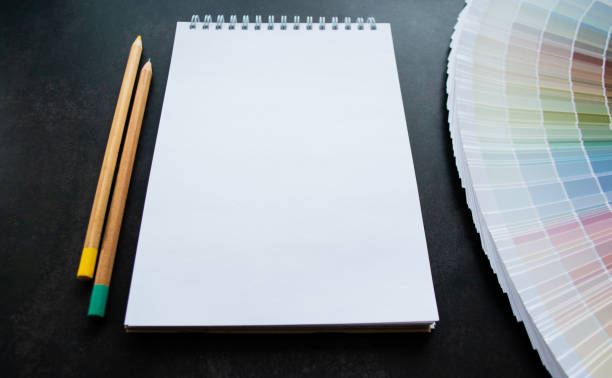 istock Fan paint samples interior design painting. Multicolored natural colors. Black background, white notebook for copy space and pencils 1406408983