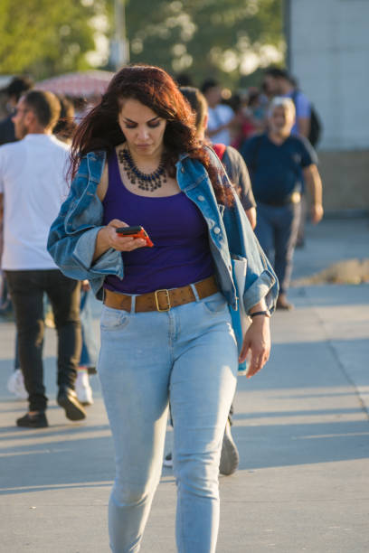 Istanbul, Turkey - July 01, 2022: People walking on Kadikoy square Istanbul, Turkey. One young woman talking on mobile phone and walking slowly.