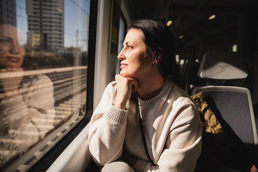 Middle aged woman sitting inside the train, looking through the window