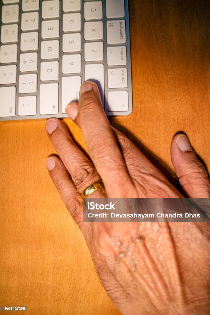 Senior Asian Hand With Fingers Crossed After Having Hit Enter on a Computer Keyboard and Taken A Chance Te left hand of a 72 year-old Asian man on an office table. He has his fingers crossed after having hit 'Enter' on the computer keyboard. He hopes all will go well. 70-79 Years Stock Photo