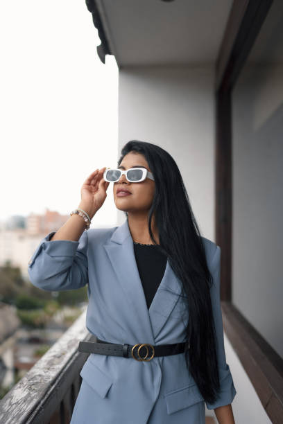 femme latine avec de longs cheveux raides, porte un blazer, une ceinture et des lunettes de soleil, mode d’affaires - glamour urban scene beautiful one person photos et images de collection