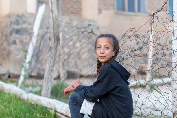 Refugee girl sitting near wire mesh fence.